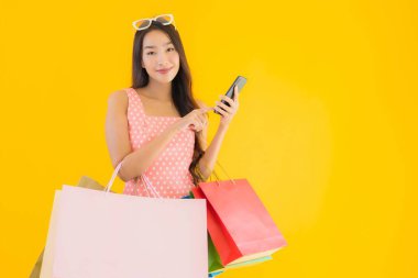 Renkli alışveriş çantalı güzel Asyalı kadın akıllı cep telefonu ve sarı izole edilmiş arka planda kredi kartı.