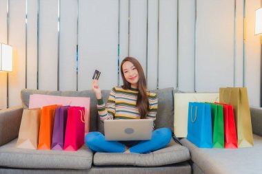 Asyalı güzel bir kadının portresi kanepeye dizüstü bilgisayar kullanıyor.