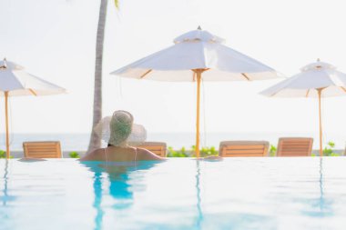 Güzel bir Asyalı kadın portresi. Tatil gezisinde deniz manzaralı açık havuz etrafında rahatça yüzebiliyor.
