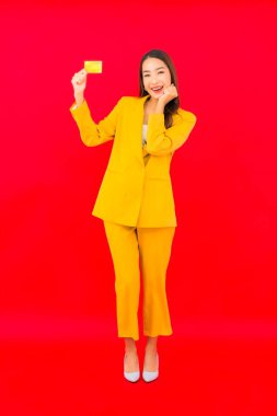 Güzel bir Asyalı kadının portresi kırmızı arka planda kredi kartıyla cep telefonu kullanıyor.