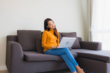 Genç Asyalı bir kadının oturma odasında çalışmak için dizüstü bilgisayar defteri kullanmasının portresi.