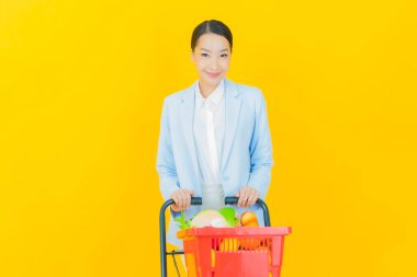 Renkli arka planda süpermarketten alınmış market sepetiyle gülümseyen güzel Asyalı kadın portresi.