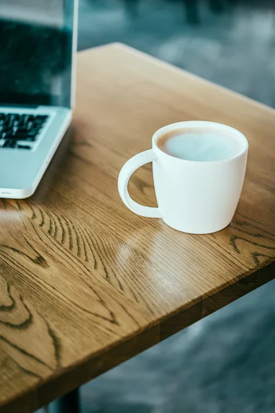 Tazza di caffè, laptop in caffetteria — Foto Stock