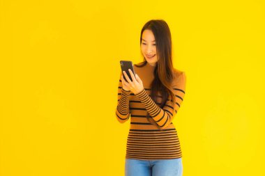 Güzel genç Asyalı kadın, sarı izole edilmiş arka planda birçok eylem içeren akıllı cep telefonu ya da cep telefonu kullanır.