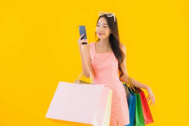 Renkli alışveriş çantalı güzel Asyalı kadın akıllı cep telefonu ve sarı izole edilmiş arka planda kredi kartı.