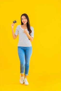 Güzel bir Asyalı kadının portresi sarı izole edilmiş arka planda online alışveriş için kredi kartını gösteriyor.