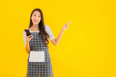 Güzel bir Asyalı kadın portresi sarı izole edilmiş arka planda akıllı cep telefonu kullanıyor.