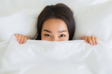 Güzel bir portre genç Asyalı kadın rahatla. Yatak odasının iç tarafında beyaz yastık battaniyesiyle mutlu bir gülümseme.