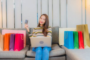 Asyalı güzel bir kadının portresi kanepeye dizüstü bilgisayar kullanıyor.