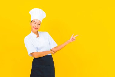 Güzel bir Asyalı kadın portresi ya da sarı izole arkaplanda şapkası olan aşçı üniforması.