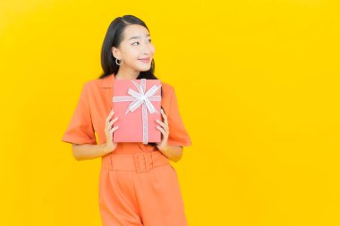 Asyalı güzel bir kadının portresi. Sarı arka planda kırmızı hediye kutusuyla gülümsüyor.