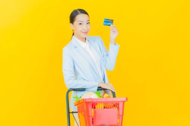 Renkli arka planda süpermarketten alınmış market sepetiyle gülümseyen güzel Asyalı kadın portresi.