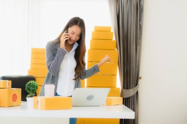 Güzel Asyalı iş kadını portresi evden bilgisayarlı cep telefonuyla karton kutuyla çevrimiçi alışveriş için hazır bekliyor.