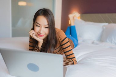 Asyalı güzel bir kadının portresi yatak odasının iç kısmında kredi kartıyla birlikte dizüstü bilgisayar kullanıyor.