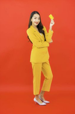 Güzel bir Asyalı kadının portresi kırmızı arka planda kredi kartıyla cep telefonu kullanıyor.