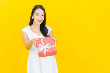 Asyalı güzel bir kadının portresi. Sarı arka planda kırmızı hediye kutusuyla gülümsüyor.