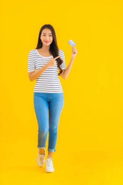 Güzel bir Asyalı kadının portresi sarı izole edilmiş arka planda online alışveriş için kredi kartını gösteriyor.