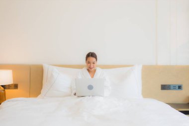 Güzel bir Asyalı kadın yatak odasının iç kısmında bilgisayar kullanıyor.