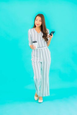 Güzel bir Asyalı kadın portresi mavi arka planda akıllı cep telefonu kullanıyor.