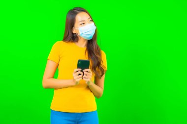 Güzel Asyalı genç bir kadının portresi, yeşil yalıtılmış arka planda kovid19 veya koronavirüsten korunmak için maske takar.