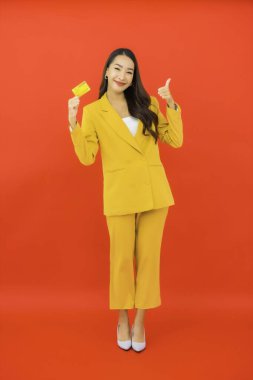 Güzel bir Asyalı kadının portresi kırmızı arka planda kredi kartıyla cep telefonu kullanıyor.