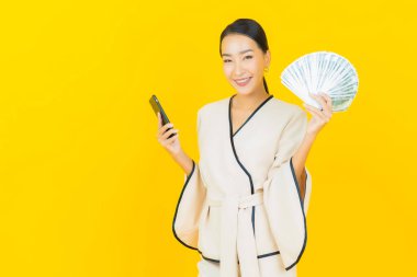 Bir sürü parası ve sarı arka planda kumbarası olan Asyalı güzel bir iş kadını portresi.