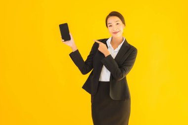 Portre güzel genç Asyalı kadın akıllı cep telefonu ve kahve fincanı ile izole edilmiş sarı arka planda