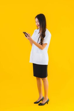 Güzel Asyalı genç doktor kadın sarı izole edilmiş arka planda akıllı cep telefonu kullanıyor.