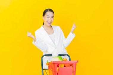 Renkli arka planda süpermarketten alınmış market sepetiyle gülümseyen güzel Asyalı kadın portresi.