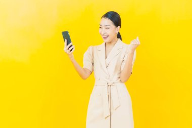 Renkli arka planda akıllı cep telefonuyla güzel Asyalı kadın gülümsemesi