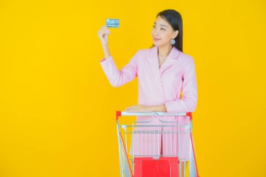 Renkli arka planda süpermarketten alınmış market sepetiyle gülümseyen güzel Asyalı kadın portresi.