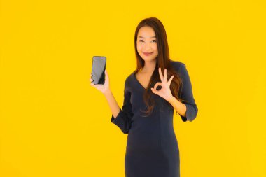 Akıllı cep telefonlu güzel Asyalı kadın portresi ya da sarı izole edilmiş arka planda cep telefonu.