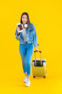 Güzel, Asyalı genç bir kadının portresi valiz ve pasaport ile seyahat, sarı izole arka planda biniş kartı.