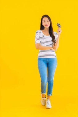 Güzel bir Asyalı kadının portresi sarı izole edilmiş arka planda online alışveriş için kredi kartını gösteriyor.