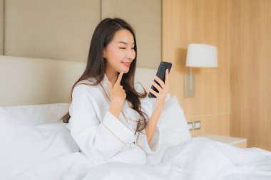 Yatak odasının içinde akıllı cep telefonlu güzel Asyalı kadın portresi.