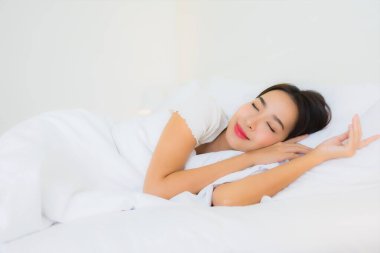 Güzel bir portre genç Asyalı kadın rahatla. Yatak odasının iç tarafında beyaz yastık battaniyesiyle mutlu bir gülümseme.