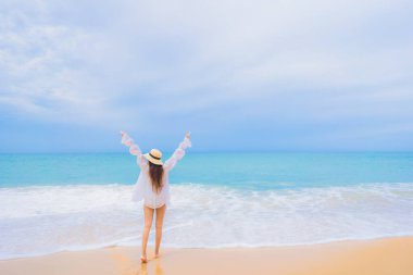 Güzel bir Asyalı kadın portresi deniz kıyısında tatil yaparken rahatça gülümser.