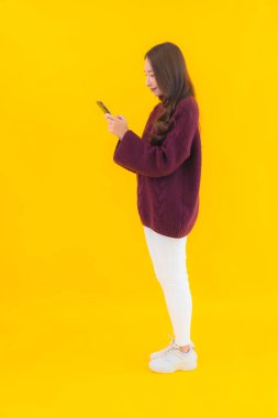 Güzel bir Asyalı kadın portresi sarı izole edilmiş arka planda akıllı cep telefonu kullanıyor.
