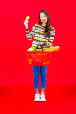 Marketten aldığı alışveriş sepetiyle kırmızı izole arka planda güzel bir Asyalı kadın portresi.