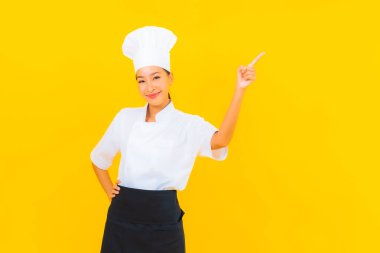 Güzel bir Asyalı kadın portresi ya da sarı izole arkaplanda şapkası olan aşçı üniforması.