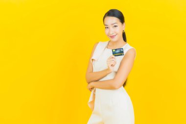 Asyalı güzel bir kadının portresi. Sarı arka planda kredi kartıyla gülümsüyor.