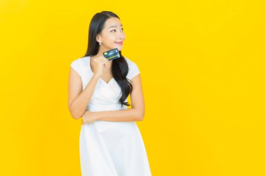 Asyalı güzel bir kadının portresi. Sarı arka planda kredi kartıyla gülümsüyor.