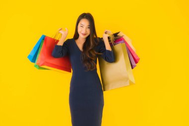Sarı izole edilmiş arka planda renkli alışveriş çantalı güzel Asyalı kadın portresi.