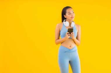 Güzel bir Asyalı kadın portresi. Sarı arka planda müzik dinlemek için akıllı telefon ve kulaklık takıyor.