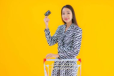 Sarı izole edilmiş arka planda market alışverişi için alışveriş arabası olan güzel Asyalı kadın portresi.