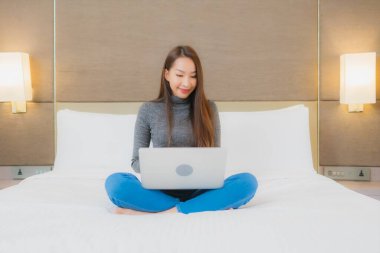 Güzel bir Asyalı kadın yatak odasının iç kısmında bilgisayar kullanıyor.