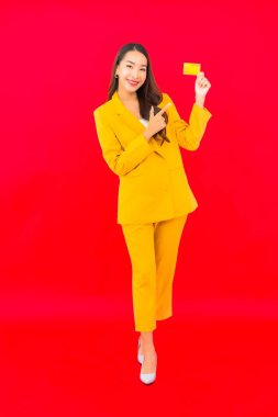 Güzel bir Asyalı kadının portresi kırmızı arka planda kredi kartıyla cep telefonu kullanıyor.