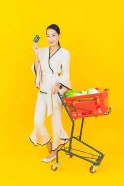 Sarı arka planda süpermarketten alışveriş sepeti almış güzel genç Asyalı kadın portresi.