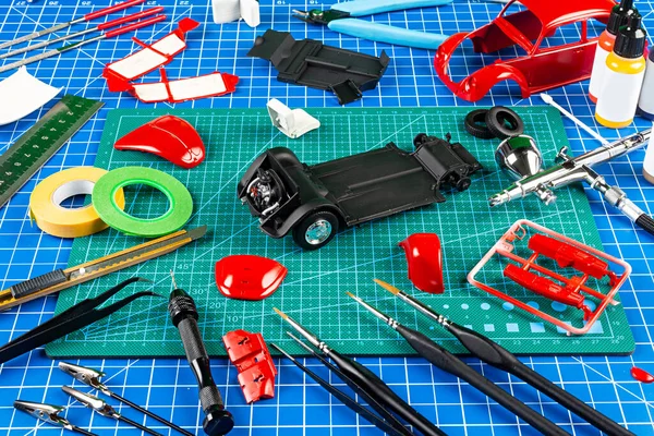 デスクトップビューアセンブリと赤のレトロなスケールモデル車の概念の背景の絵 モデリングツールエアブラシガン塗装キット部品ブルーグリーンカットマットナイフと作業机の上のブラシ — ストック写真