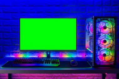 LED hafif tuğla duvarın önünde yeşil ekran fotokopi alanı olan klavye fare monitörlü renkli, parlak, rgb oyun bilgisayarı. Bilgisayar donanım oyunları oynuyor